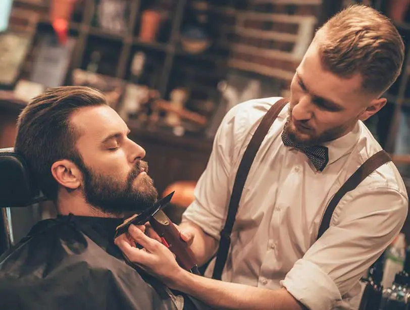 A man getting his beard trimmed by another man.