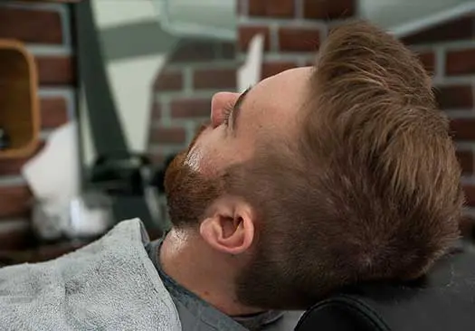 A man with a beard is getting his hair cut